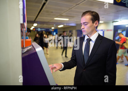 Giovane imprenditore tramite bancomat presso stazione ferroviaria Foto Stock