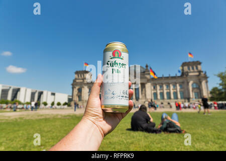 Berlino, Germania - luglio 14,2018: bianco uomo mano trattiene un può di Lubzer birra tedesca closeup con Bundestag o edificio del Reichstag in background. Foto Stock