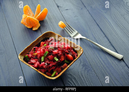 Ciotola di insalata russa Insalata di barbabietole rosse, verze, carote, potatoe e cipolla verde, con scafo in mandarino la forcella sull'azzurro del tavolo di legno, se Foto Stock