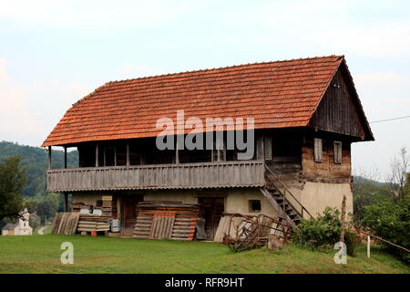 Grande Vecchia casa in legno con fatiscenti incrinato schede e finestre con portico anteriore sopra gli strumenti utilizzati e tavole di legno coperta con tegole del tetto Foto Stock