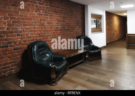Interno con due poltrone di pelle nera e un tavolo da caffè contro in rosso di un muro di mattoni. Foto Stock