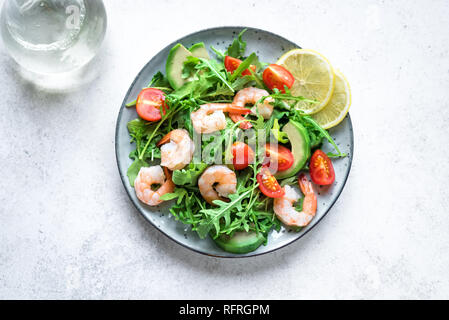 Avocado insalata di gamberetti con rucola e pomodori in pietra bianca di sfondo, copia dello spazio. Dieta sana insalata verde con gamberi, avocado, ciliegia Foto Stock
