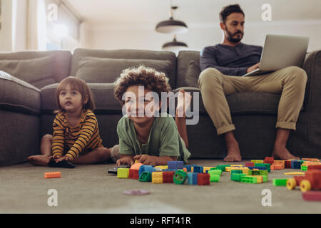 Sorridere i bambini giocando con la costruzione di blocchi e guardare la televisione a casa. L'uomo baby i suoi bambini e lavora da casa. Foto Stock