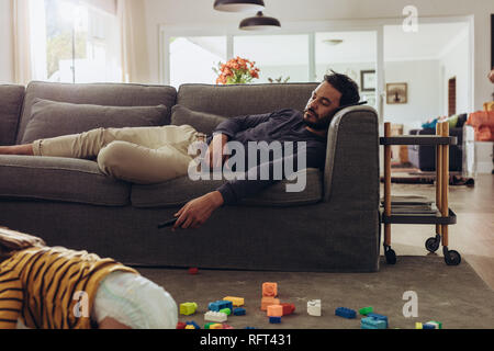 L'uomo rilassante sul lettino con il suo ragazzo giocando sul pavimento. Kid giocando sul pavimento con blocchi di costruzione mentre il padre è dormire sul divano. Foto Stock