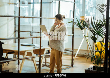 Donna incinta che indossa un maglione beige avente la video chat su laptop Foto Stock