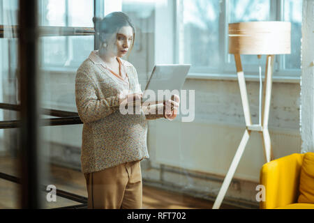 Donna incinta che indossa pantaloni beige e un maglione holding laptop Foto Stock