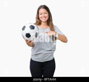 Giovane bella bruna donna azienda soccer football palla su sfondo isolato con sorpresa faccia puntare il dito a se stesso Foto Stock