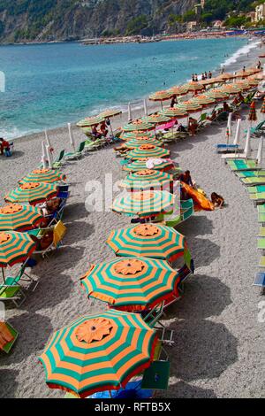 Arancione e verde listati ombrelloni da spiaggia su una popolare spiaggia italiana Foto Stock