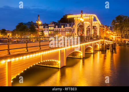 Illuminata Magere Brug (Skinny Bridge) di notte che attraversano il fiume Amstel di Amsterdam, Olanda Settentrionale, Paesi Bassi, Europa Foto Stock