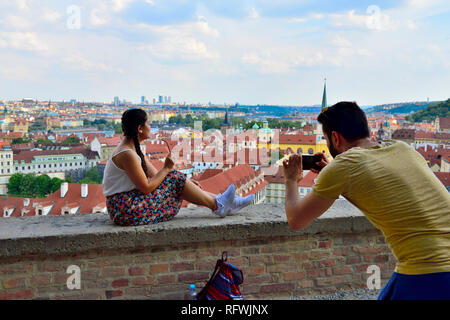 Affacciata sulla città di Praga dal castello con uomo prendendo la fotografia della donna seduta sulla parete Foto Stock