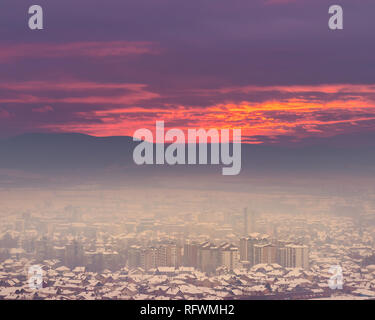 Masterizzazione di incredibile Cielo di tramonto sulle Misty, nebbia, golden cityscape di Pirot con rosa e viola il cielo e edifici coperti di smog Foto Stock