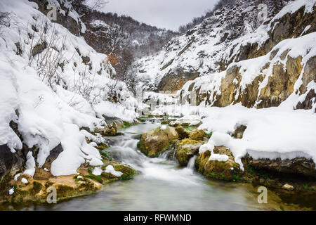 I colori vivaci di una mountain creek cascading attraverso il canyon coperto di neve Foto Stock