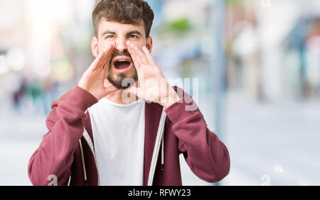 Giovane uomo bello su isolati che urlava arrabbiato ad alto volume con Mani sulla bocca Foto Stock