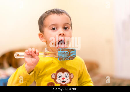 Bambino felice lambisce un cucchiaio con il cioccolato. Felice ragazzo di mangiare una torta al cioccolato. Funny baby mangiare il cioccolato con un cucchiaio Foto Stock