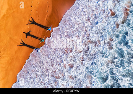 Tre attivo esercizio di persone che guardano verso il rotolamento surf onde dell oceano Pacifico sul telecomando appartata spiaggia di sabbia del Nord di Sydney nel caldo sole lig Foto Stock