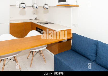 Moderne in legno marrone arancione caratteristiche cucina Armadi in piccolo appartamento studio sgabello da bar contatore di interior design e nessuno sul divano blu in stile minimalista Foto Stock