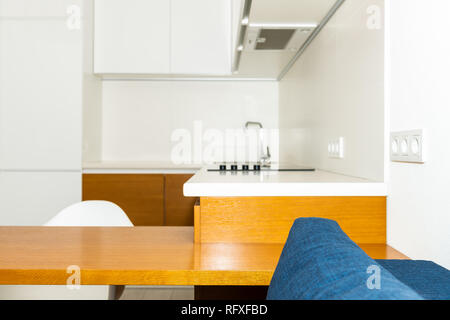 Moderne in legno marrone arancione mobili da cucina nel piccolo appartamento studio sgabello da bar contatore di interior design e nessuno sul divano blu in casa minimalista Foto Stock