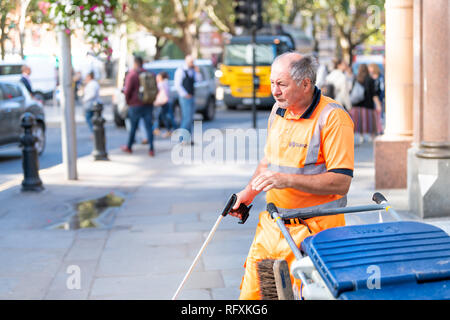 London, Regno Unito - 13 Settembre 2018: Senior British uomo lavoratore cleaner in arancione una pulitura uniforme nel cestino della spazzatura strade di Chelsea con attrezzo su strada pavem Foto Stock