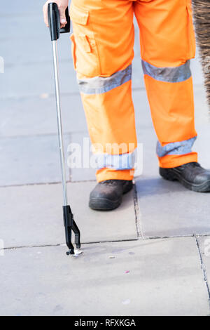 L'uomo lavoratore cleaner in arancione una pulitura uniforme nel cestino della spazzatura strade di Londra con strumento di selezione sulla pavimentazione stradale durante il giorno Foto Stock