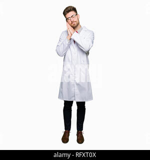 Giovane scienziato bello uomo che indossa gli occhiali sleeping stanchi di sognare e in posa con le mani insieme mentre sorridente con gli occhi chiusi. Foto Stock