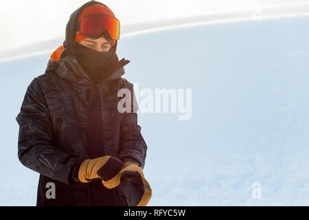 Giovani snowboarder in sportswear mettendo sul suo i guanti prima di snowboard Foto Stock