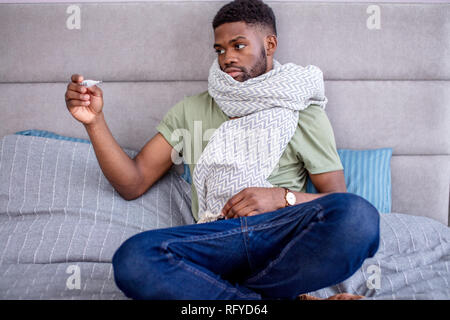 Triste ill uomo africano sensazione di malessere, di stare a casa a letto con il tè caldo Foto Stock