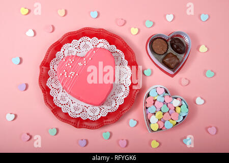 Vista superiore del cuore sulla torta rossa piastra decorativa con Centrino bianco scatola di cuori di caramelle e cioccolatini su sfondo rosa. Foto Stock