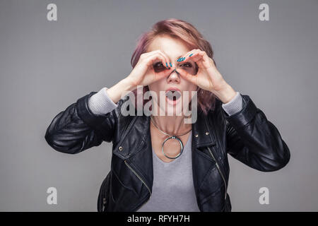 Ritratto di sorpresa bellissima ragazza con breve acconciatura e trucco in stile casual nero giacca in pelle in piedi e guardando nel gesto binoculare. i Foto Stock