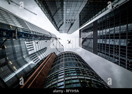 Silhouette di un aereo a reazione volare basso su tre diversi tipi di architettura con edifici di uffici commerciali esterno in Londra Foto Stock