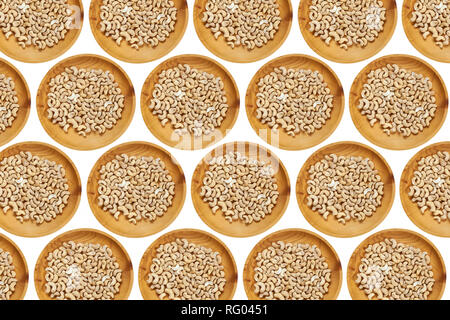 Sbucciate anacardi in un ceppo di legno di pino sulla piastra bianca di sfondo isolato. Fila di coppe con noci di acagiù, vista dall'alto. Sbucciate anacardi pattern Foto Stock