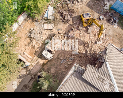 Vista aerea del sito di demolizione con metà diroccato vecchio edificio, giallo escavatore e dumper Foto Stock