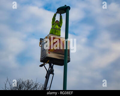 Un uomo su un argano idraulico effettuando una riparazione su un lampione post Foto Stock