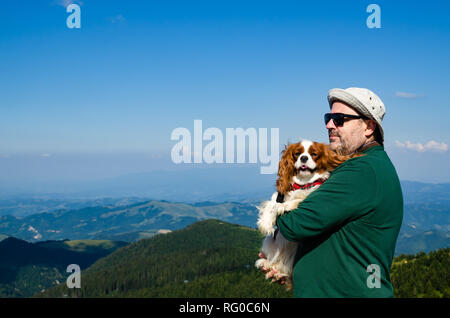 Uomo con il suo cane - Cavalier King Charles Spaniel - in un paesaggio di montagna Foto Stock