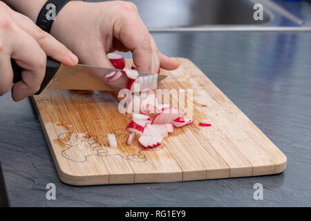 Le mani di donne tagliano ravanelli e verdure su scheda Foto Stock