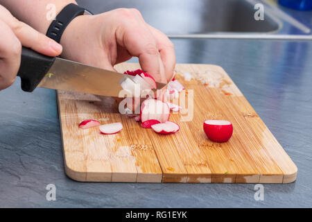 Le mani di donne tagliano ravanelli e verdure su scheda Foto Stock