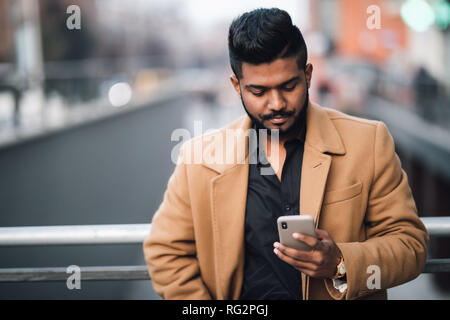 Ritratto di barbuto uomo indiano nel rivestire utilizzare sul telefono su strada Foto Stock