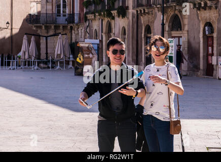 Ritratto di maschio e femmina di turisti in piazza cittadina, uomo azienda selfie stick, ridere, Ortigia, Siracusa, Sicilia, Italia, Europa Foto Stock