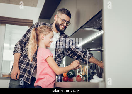 Bambina e i suoi alti padre barbuto in occhiali di trascorrere del tempo in cucina Foto Stock