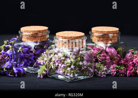 Set di erbe curative.di timo fresco, salvia e trifoglio rosso cantato in bottiglia. Medicina alternativa concetto su un tavolo di legno su sfondo nero(selective foc Foto Stock