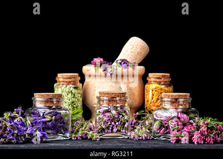 Set di erbe curative.di timo fresco, salvia e trifoglio rosso cantato in bottiglia. Medicina alternativa concetto su un tavolo di legno su sfondo nero(selective foc Foto Stock
