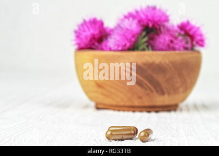 Silybum marianum (cardo) pillole e fiori in un vaso di legno.Uno degli impieghi più comuni di cardo mariano è per trattare problemi di fegato.alternativa Foto Stock