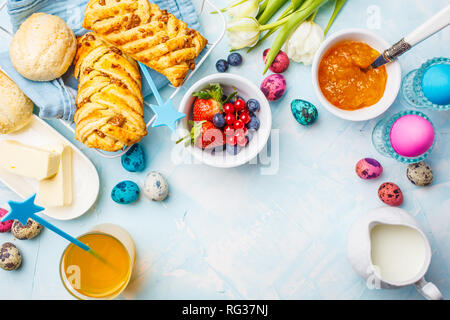 Colazione di Pasqua la tabella. Uova colorate, panini, latte, succhi di frutta e marmellata. Sfondo blu, vista dall'alto, alimentare il telaio. Foto Stock