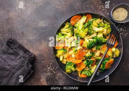 Vegan wok stir fry con broccoli e carote nel piatto nero, backgrond scuro. Foto Stock