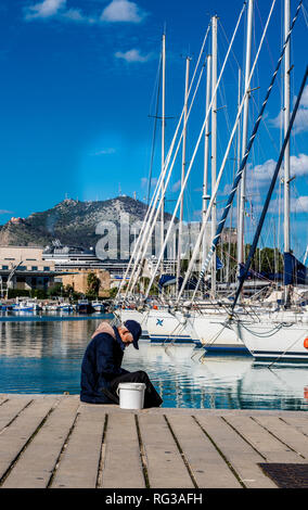 Uomo seduto sul dock in porto, barche ormeggiate in background, della città di Palermo, Sicilia, Italia, Europa Foto Stock