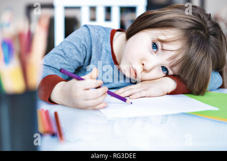 Ritratto Kid ragazza con matita colorata seduto da solo e guardando fuori con faccia annoiata, bambini in età prescolare che stabilisce a testa in giù sulla tavola con la faccia triste