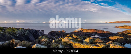 L'isola di Arran in inverni prima neve del 2019 da un lichene roccioso litorale coperto e una drammatica del cielo. Un ampio panorama angolato Foto Stock