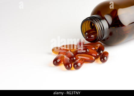 Vista ravvicinata di orange pillole o capsule di lecitina in un flacone di vetro scuro su sfondo bianco con spazio per il testo Foto Stock