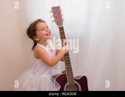 Poco divertente sorridente ragazza in costume di fiocco di neve con la chitarra acustica nella scuola musicale Foto Stock