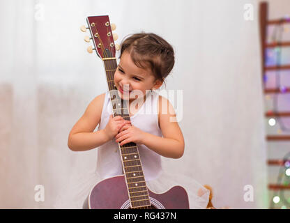 Poco divertente sorridente ragazza in costume di fiocco di neve con la chitarra acustica nella scuola musicale Foto Stock