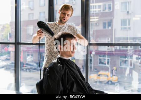 Uomo bello al parrucchiere soffiare la sua asciugatura Capelli Foto Stock